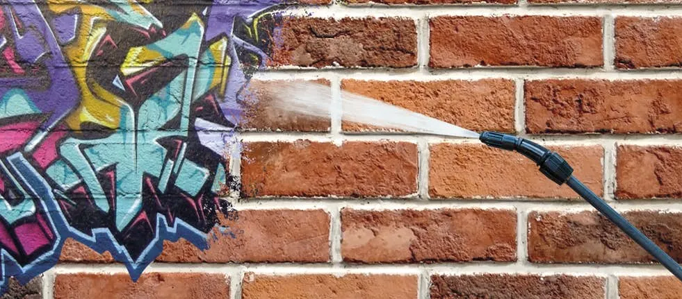 high-pressure water wand removing spray paint graffiti from a red brick wall