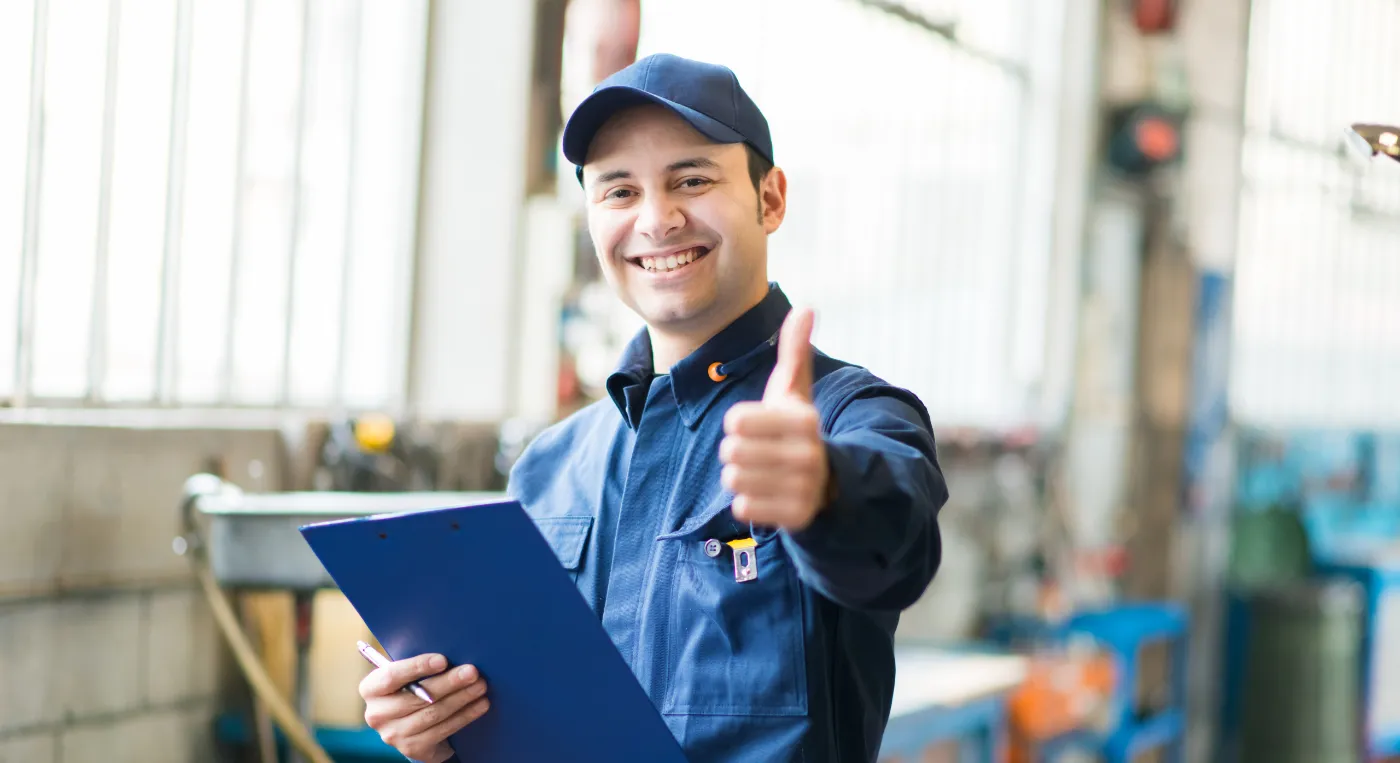 smiling worker in blue uniform holding a clipboard in an industrial setting